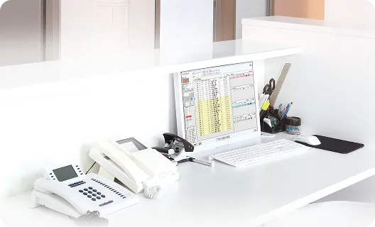 予約管理システムが表示されたパソコンと電話が置かれた、白い受付デスク
