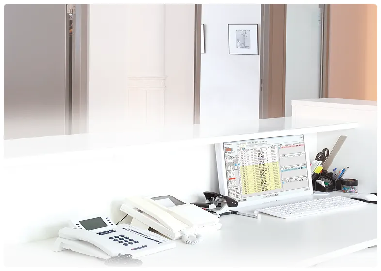 予約管理システムが表示されたパソコンと電話が置かれた、白い受付デスク